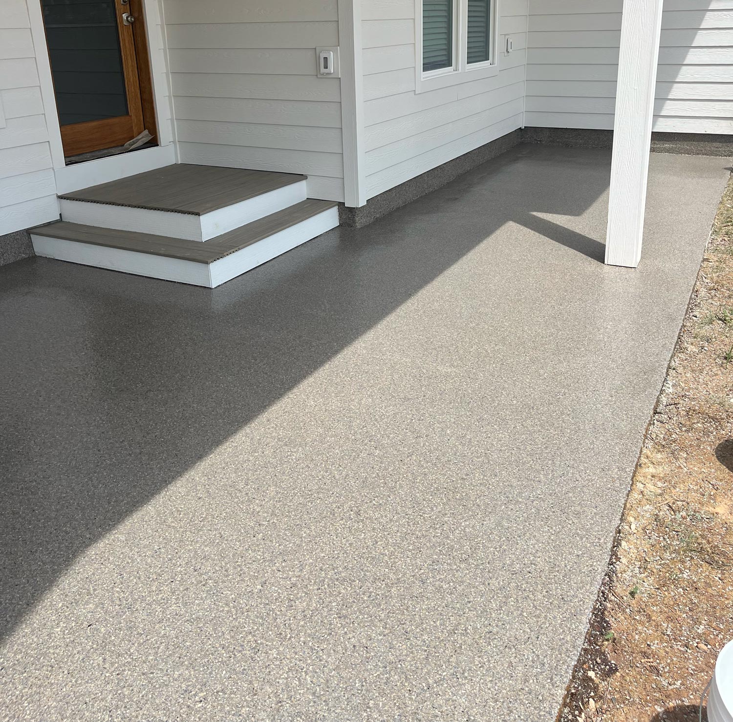 Freshly coated gray garage floor with a speckled finish beside a white house and small set of steps.