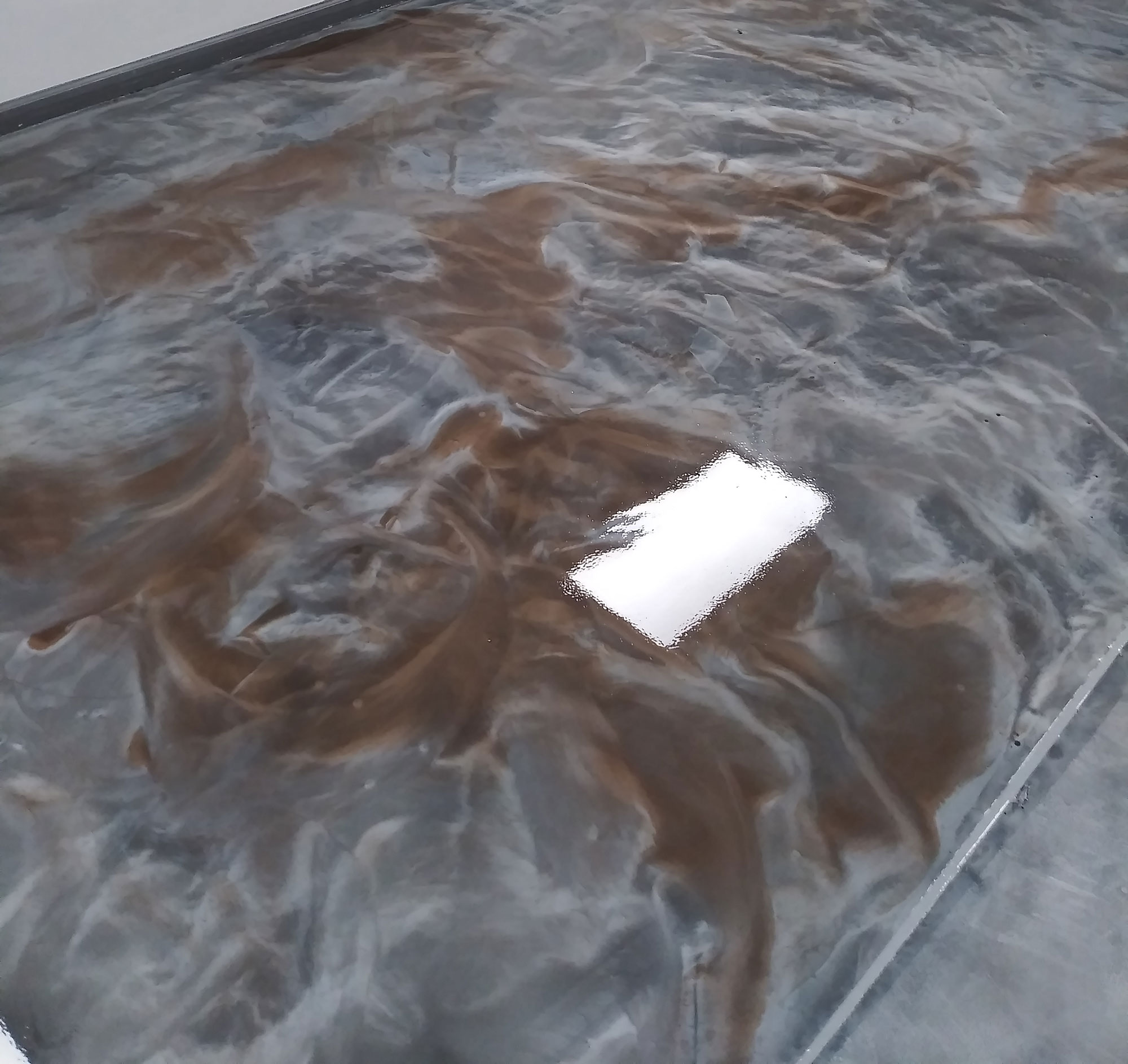 Swirled brown and gray epoxy floor with a glossy, marbled finish, reflecting a ceiling light.